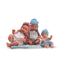 Three vinyl dolls in romper suits and hats sit on a floral pillow, showcasing playful expressions and lifelike details.