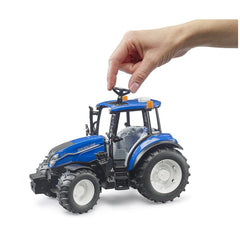 Hand interacting with a blue New Holland T5.120 toy tractor featuring realistic details and rugged tires.