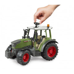 Child's hand steering a green Bruder Fendt Vario 211 toy tractor with red wheels on a white background.