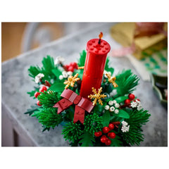 LEGO Christmas Table Decoration featuring a tall red candle at the center, surrounded by vibrant green foliage, golden stars, red berries, and a decorative bow.