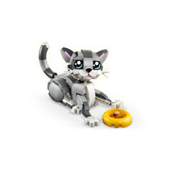A gray and white LEGO® Creator 3in1 Playful Cat construction set, sitting playfully beside a yellow toy bowl filled with brown kibble. The cat features large, expressive blue eyes, a pink nose, and a curved tail, inviting imaginative play.