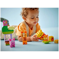 A young child sitting on a light blue surface interacts with colorful LEGO® DUPLO® blocks, including Winnie the Pooh, Tigger, and Piglet figures. Bright building pieces depict a birthday theme, with a small green lattice structure and a cake with candles. The child's expression is focused and playful, emphasizing imaginative play.