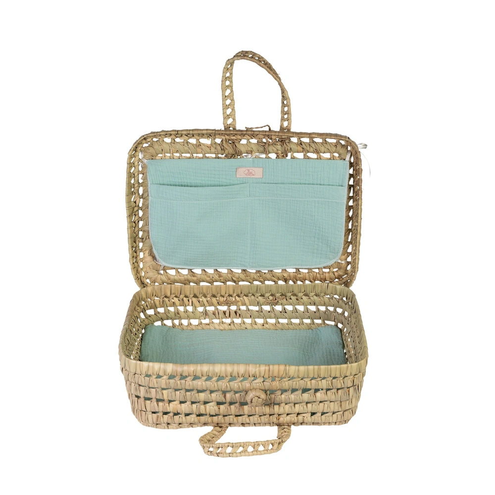 Open palm leaf suitcase with green muslin lining, featuring a woven handle and organizer pocket inside.