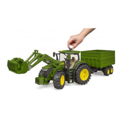 Green John Deere toy tractor with front loader and tandem axle trailer, hand adjusting roof.