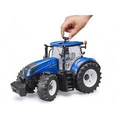 Hand operating blue BRUDER New Holland T7.315 toy tractor with large tires, clear cab, and detailed exterior.