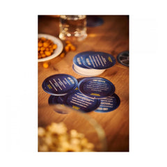 Cine Buster coasters in blue and white on a wooden table with a glass of water and a plate of nuts.
