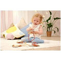 Eichhorn String Game showing a child tying a knot, surrounded by a cozy room with colorful decor and soft lighting.