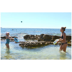 Gowi Active Hand Trampoline Game features two girls playing with blue and white plastic frisbees on a sandy beach.