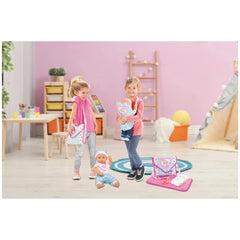 Heless doll carrier featuring unicorn Emil and fairy Emma, with young girls in casual attire in a pink-themed playroom.