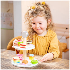 New Classic Toys Cake Stand Set with colorful plastic cupcakes, decorations, and a wooden table in a lively scene.