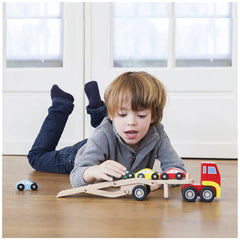 Car transporter toy set with blue car and red-yellow truck, child playing on wooden floor wearing blue jeans and gray sweater