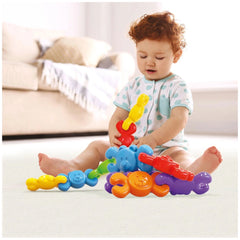 Quercetti Orsetti baby activity toy, colorful interlocking pieces with a smiling face, held by a child in pajamas on carpet.