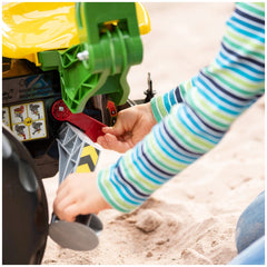 Rollybackhoe John Deere toy excavator with a red lever being operated by hands on a sandy surface.