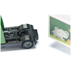 Articulated truck with trailer in black metallic finish alongside a cardboard elephant cutout on green grass.