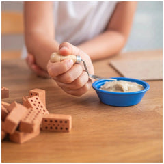 Teifoc creative box with colorful Lego bricks, a blue bowl, and a child's hands holding a spoon on a wooden surface.