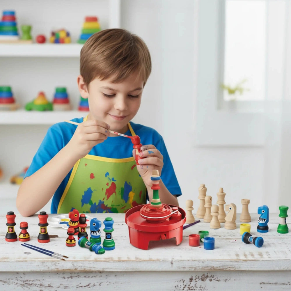 Young boy in a blue apron painting a wooden spindle red with a brush, surrounded by colorful wooden toys on a light wood tabl