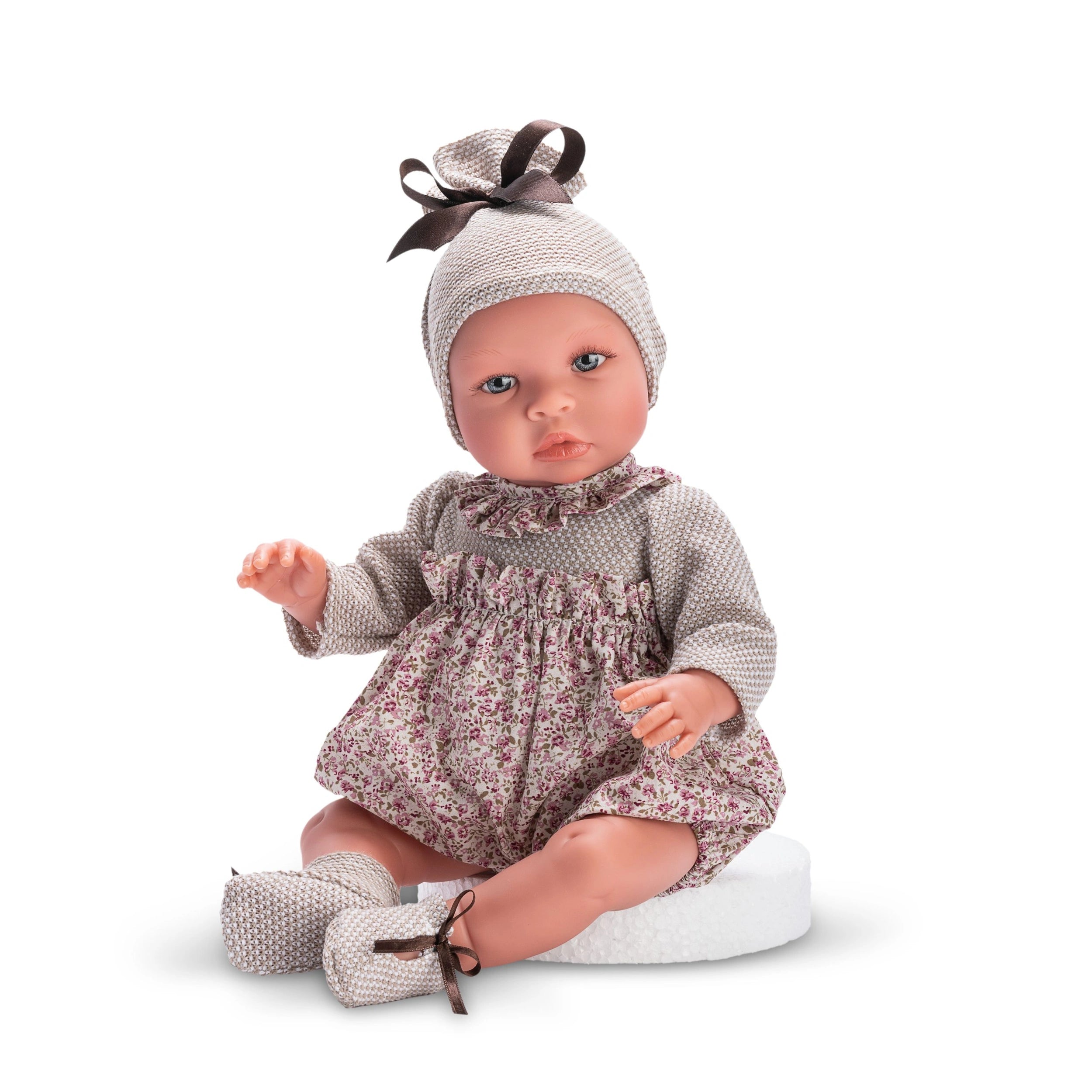 ASI Dolls Leo Romper from Martina Collection, 46 cm, with floral outfit and hat, expressive eyes, seated on a white surface.