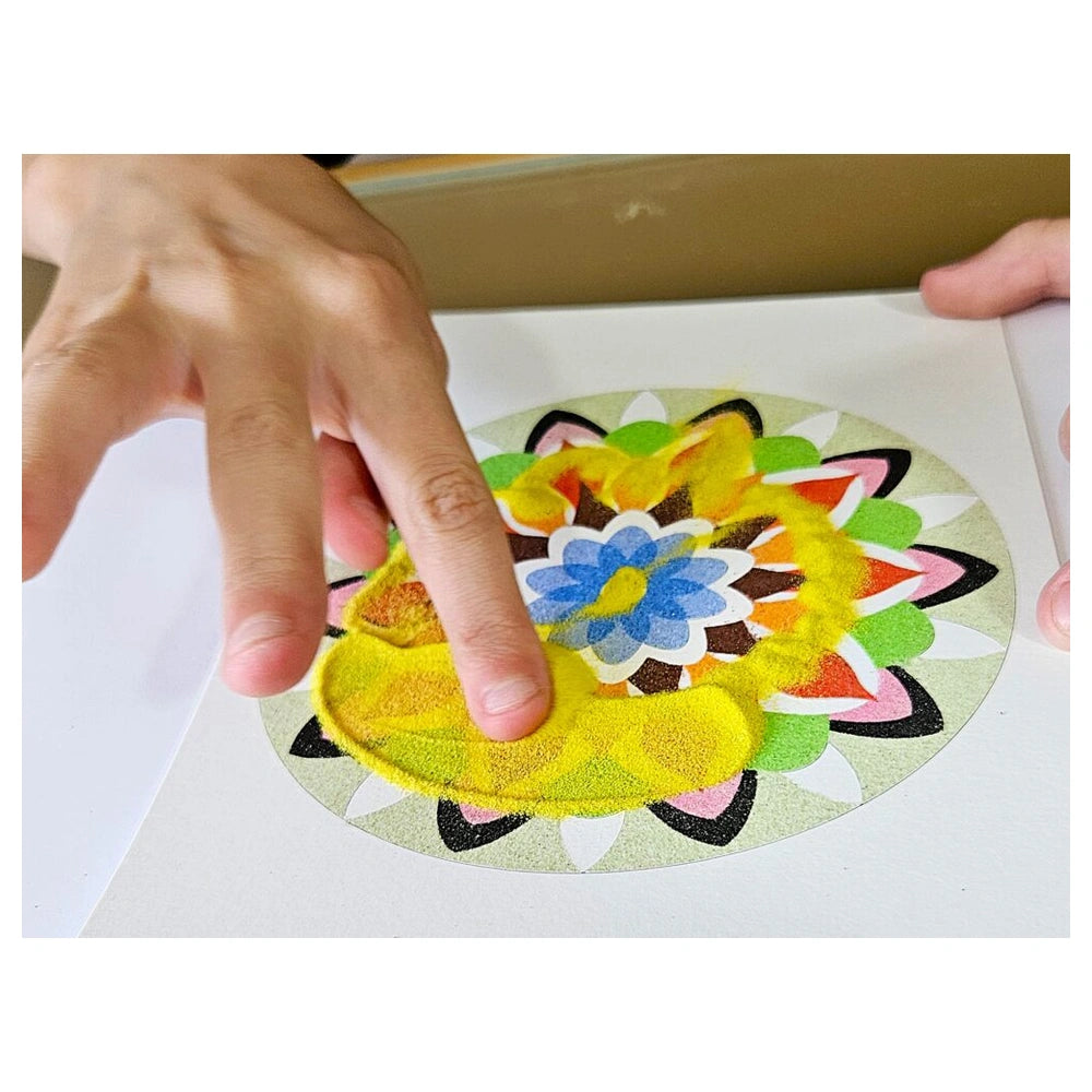 Colorful circular sand art mandala being held by a person's hand, showcasing vibrant designs on a white surface.