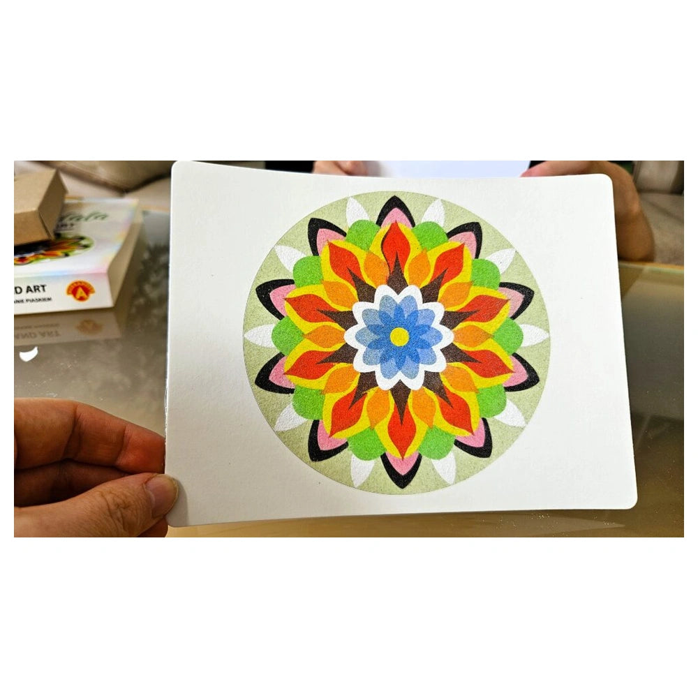 Sand Art Mandala features a vibrant, symmetrical floral pattern in various colors held by a hand indoors.