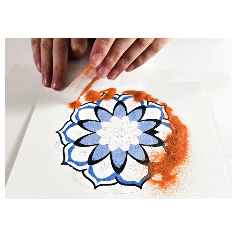 Sand Art Mandala kit features a hand painting a swirling red-orange pattern on white paper with a brush.