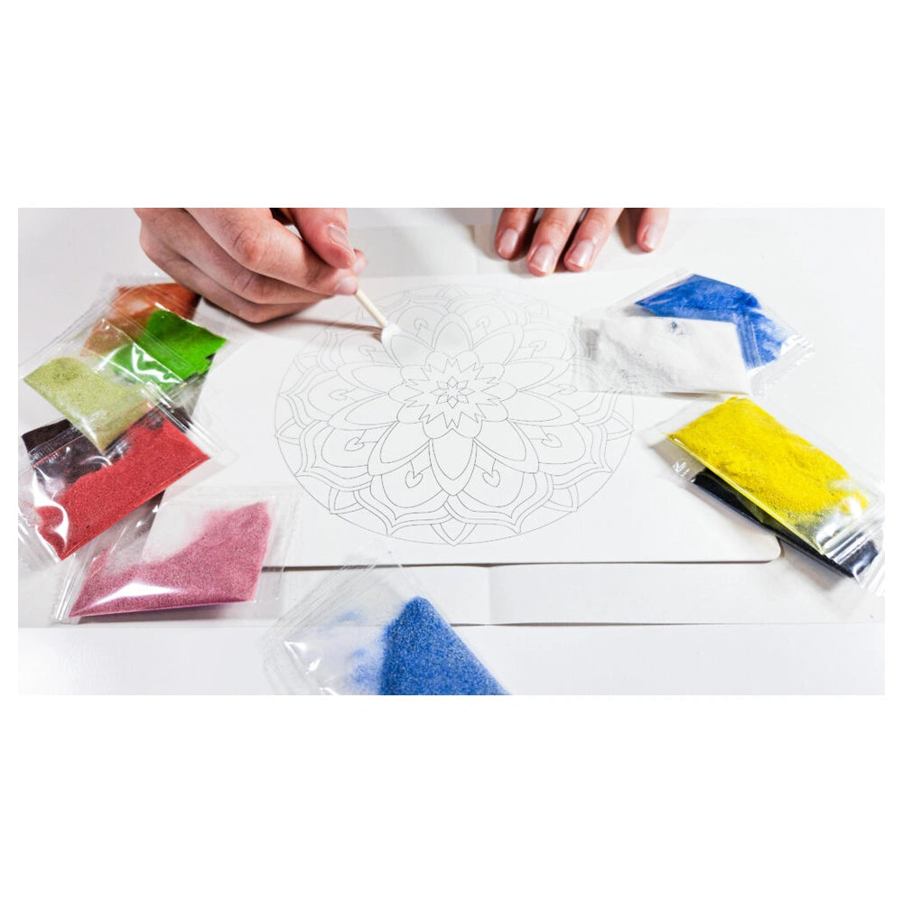 Sand art mandala crafting activity with colorful powders, a paintbrush, and a floral design on cardstock.