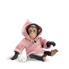Chimpanzee doll in pink hooded dress, seated with a pacifier nearby, lifelike facial features and expressive eyes.