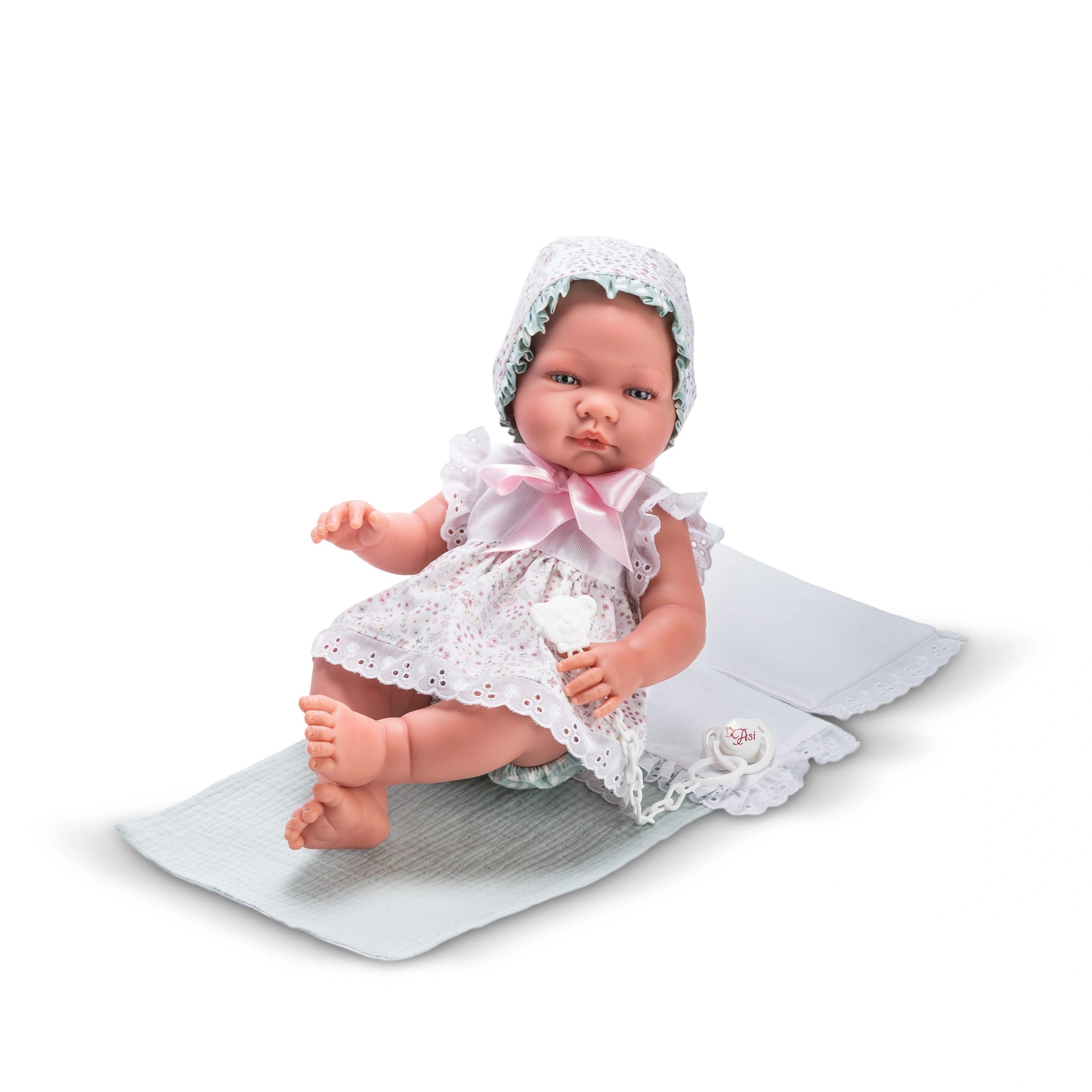 María doll in floral Cloe dress with bonnet, lying on white mat.
