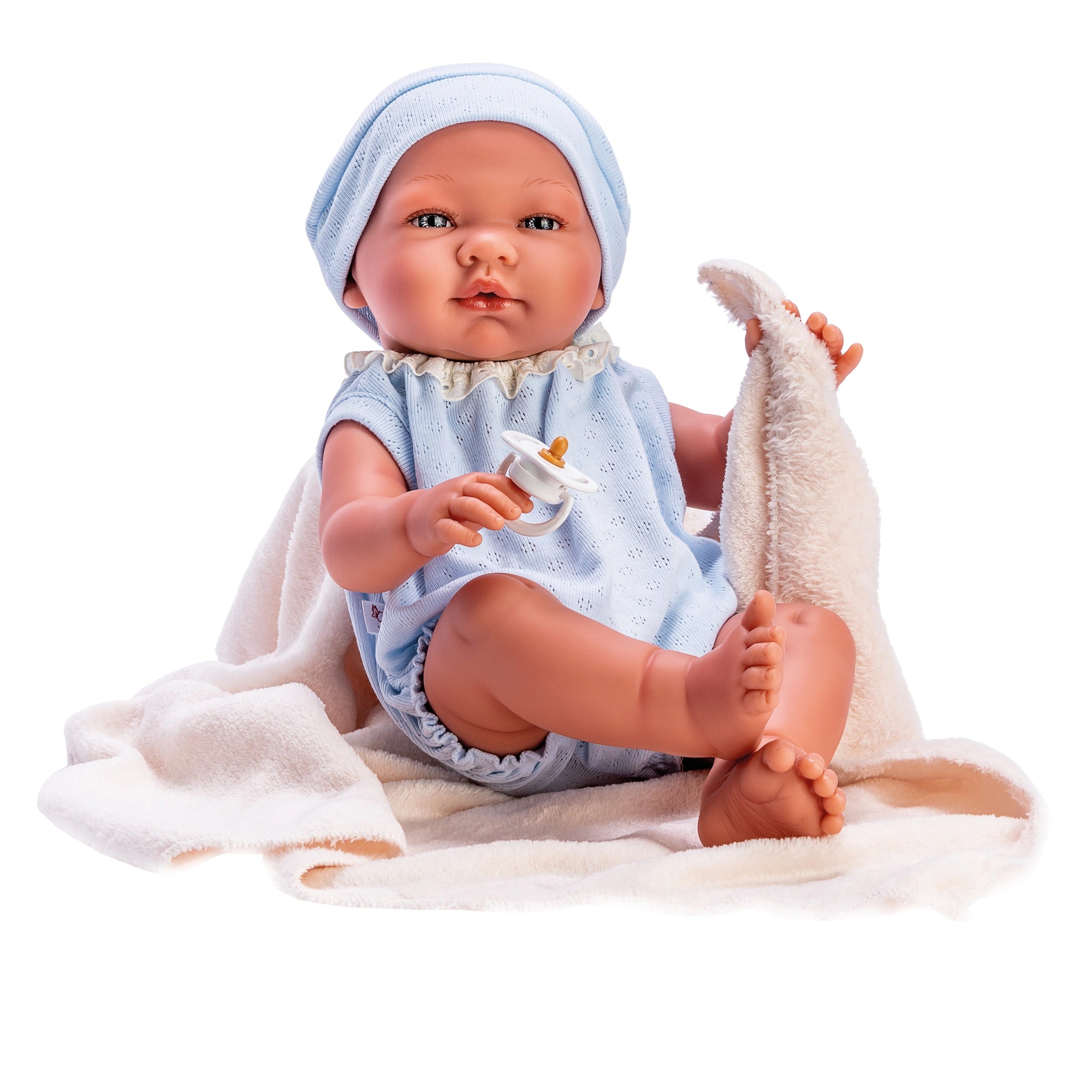 Charming Asi Dolls Pablo, 43 cm, in blue knitted body and cap, holding a pacifier, seated on a beige blanket.