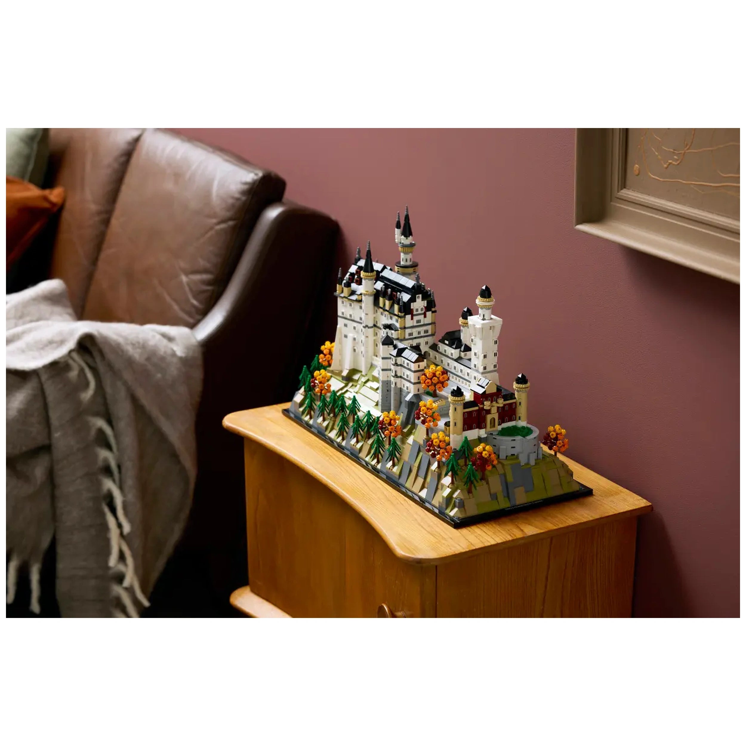 LEGO Neuschwanstein Castle model displayed on a wooden table, featuring intricate white towers, black roofs, and colorful foliage in a cozy living room setting.