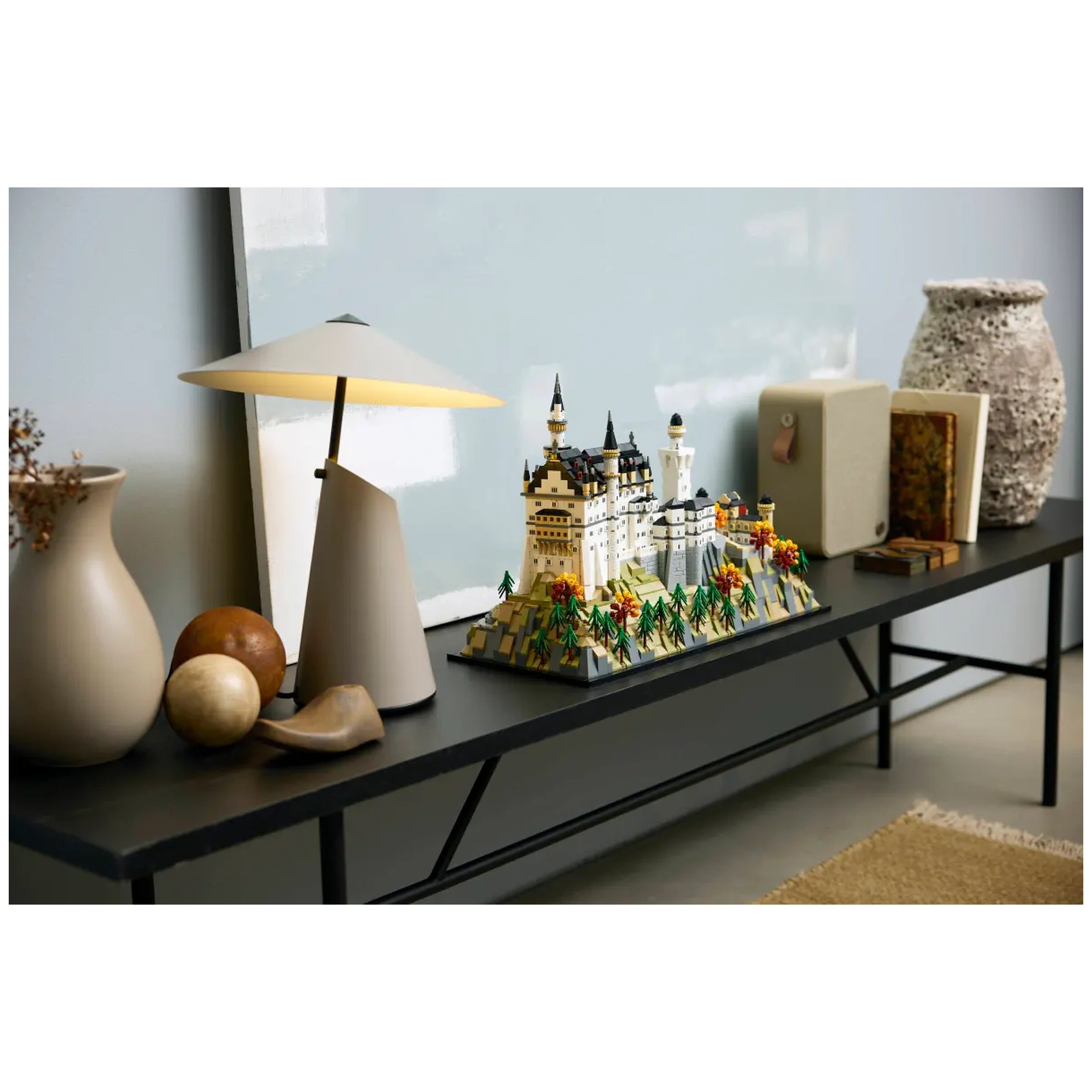 LEGO Architecture Neuschwanstein Castle set displayed on a sleek black table with decorative items, including a modern lamp, wooden spheres, and a textured vase.