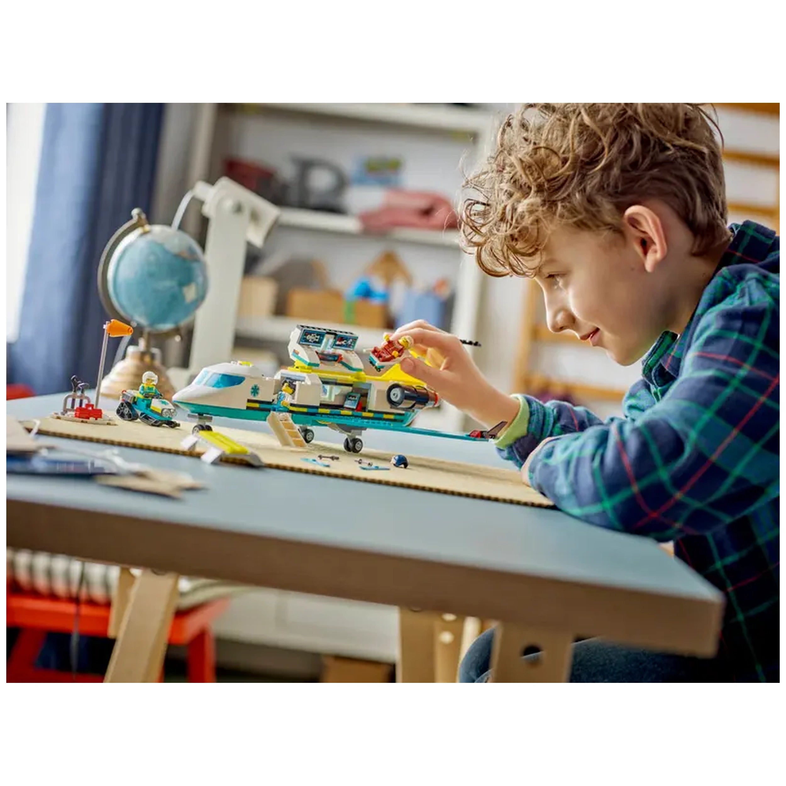 A child with curly hair plays on a table, interacting with the LEGO® Emergency Air Ambulance Plane set, featuring a detailed model and minifigures.