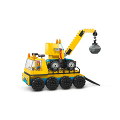 A yellow construction truck equipped with a wrecking ball crane, featuring four large wheels, a driver's cabin with a minifigure, and bright safety lights. The crane extends upward, holding a gray wrecking ball, ready for demolition play.