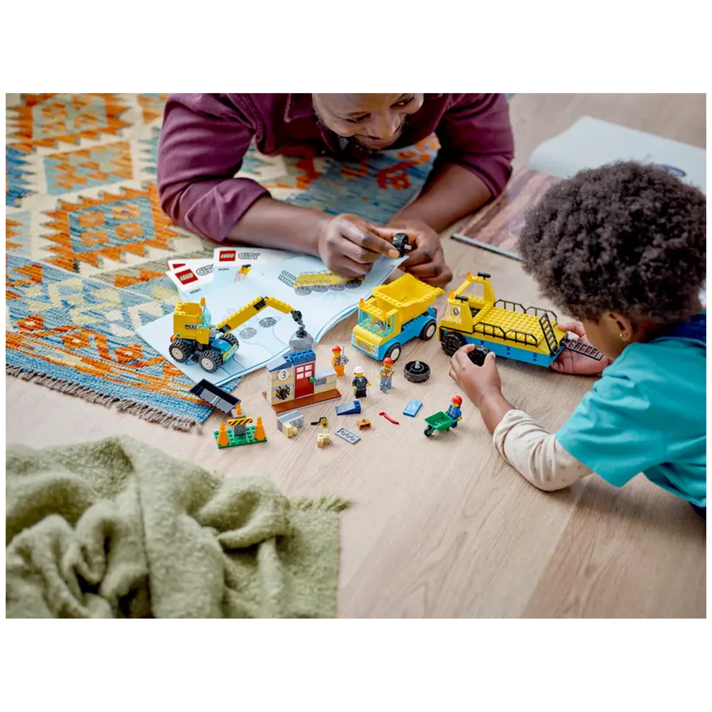 Two children play with LEGO® construction toys on a colorful rug, assembling a dump truck, crane, and minifigures, surrounded by building instructions and blocks.