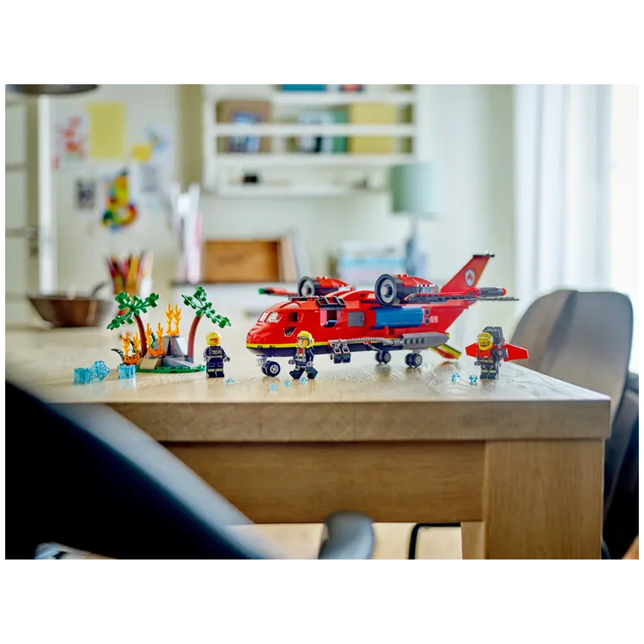 LEGO City Fire Rescue Plane on a wooden table, featuring a red twin-engine aircraft, three firefighter minifigures, and a small fire scene with flames and trees.