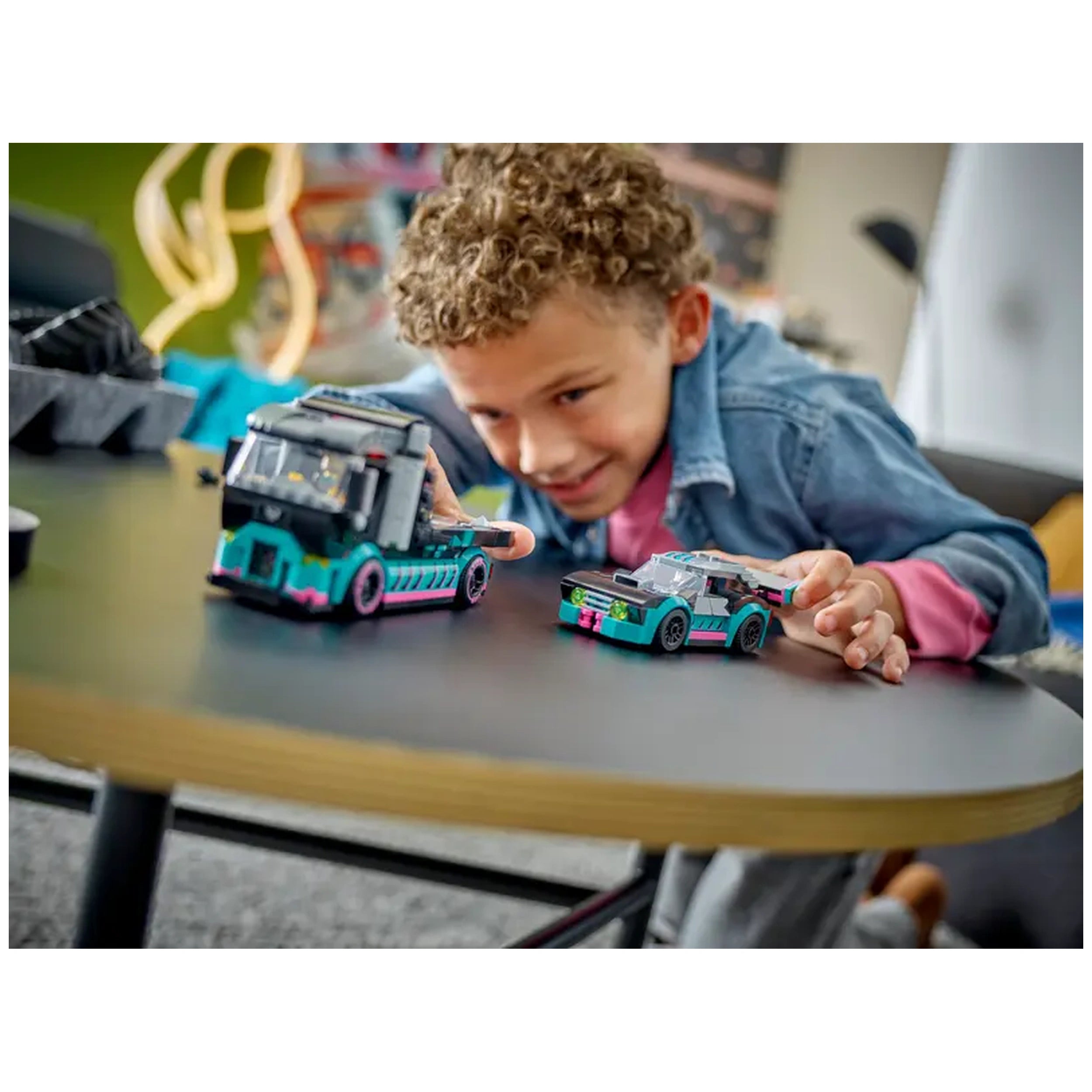 A child with curly hair leans forward on a tabletop, excitedly playing with a colorful LEGO® city race car and a car carrier truck, showcasing vibrant hues of blue, pink, and black.