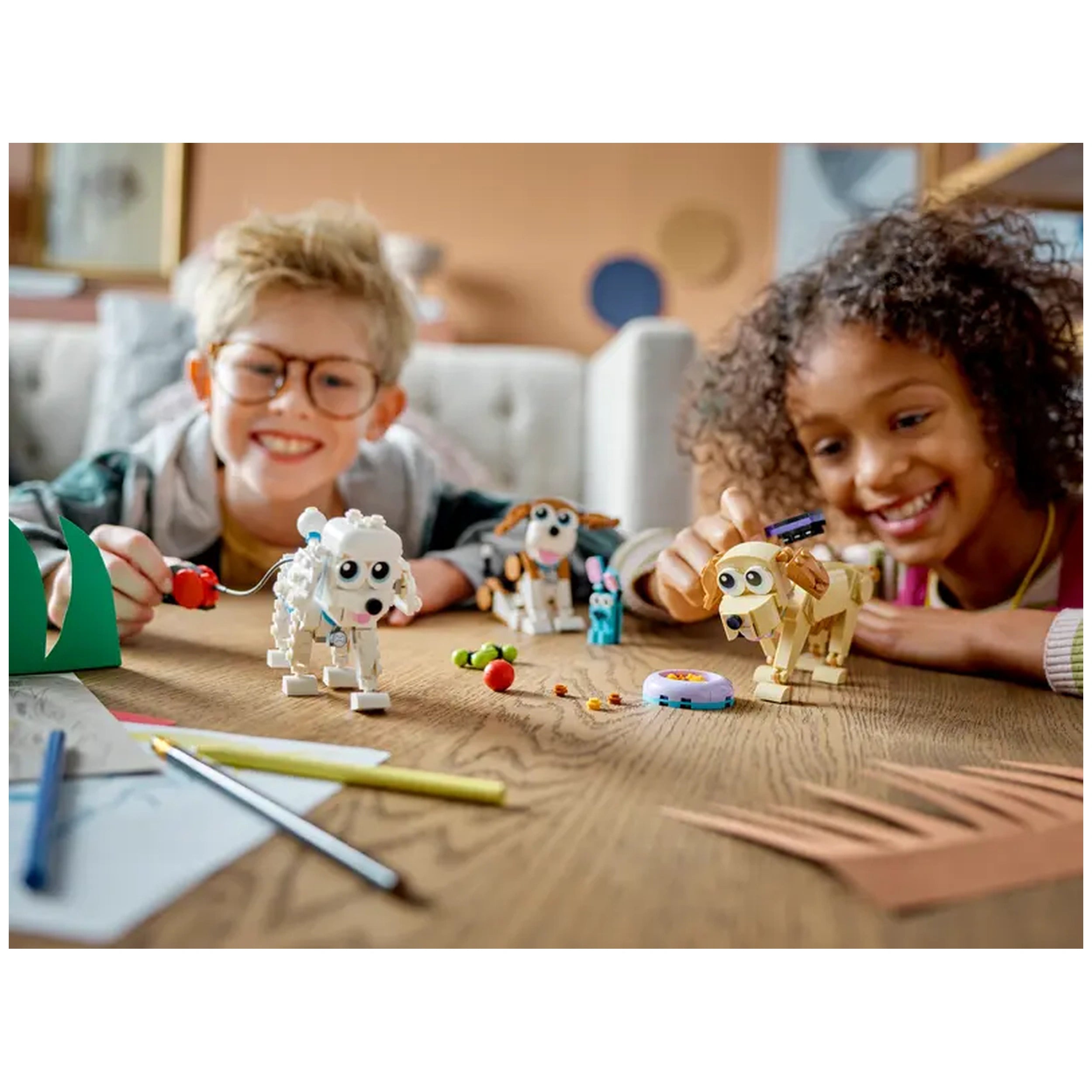 Two children engaged in play with LEGO® Creator 3in1 Adorable Dogs on a wooden table. A white dog and a brown dog are among colorful accessories like a toy rabbit and a food bowl.