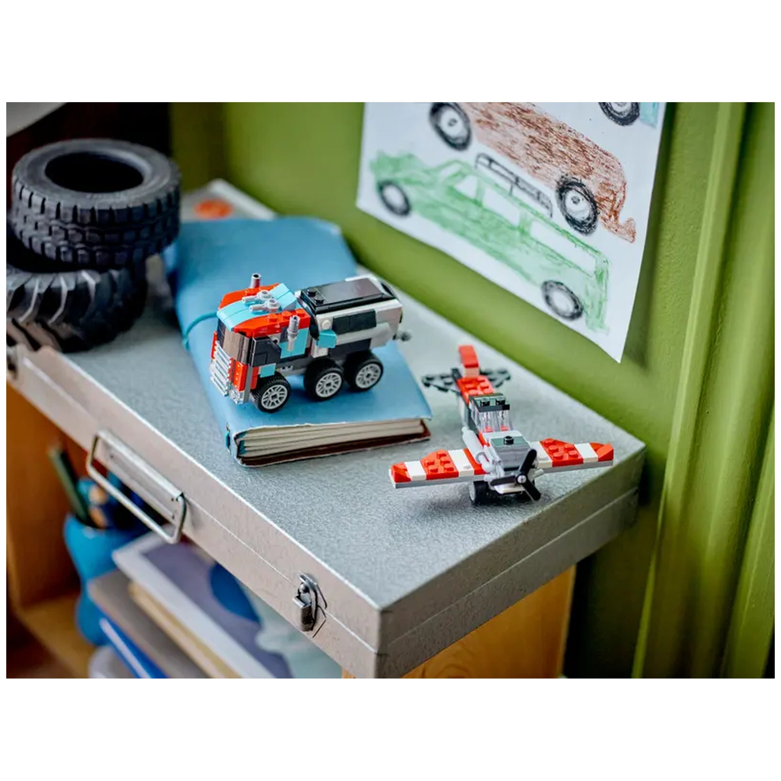 Colorful LEGO® Creator model of a flatbed truck and helicopter on a silver desk, with a blue book and toy tires in the background.