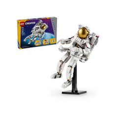 LEGO Creator Space Astronaut construction set featuring a detailed white astronaut figure with a gold visor and jet propulsion backpack, displayed on a black stand. The colorful box showcasing the 3-in-1 build options is in the background, with a cosmic theme and age recommendation for 9+.