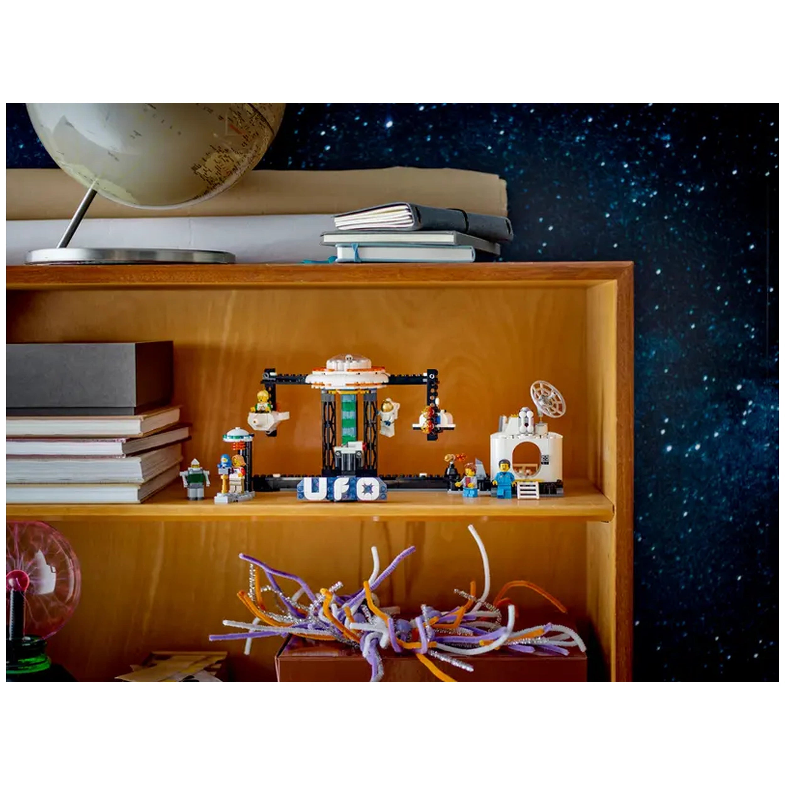 Colorful LEGO® Creator 3in1 Space Roller Coaster set displayed on a wooden shelf, featuring whimsical figures and a UFO design against a starry backdrop.