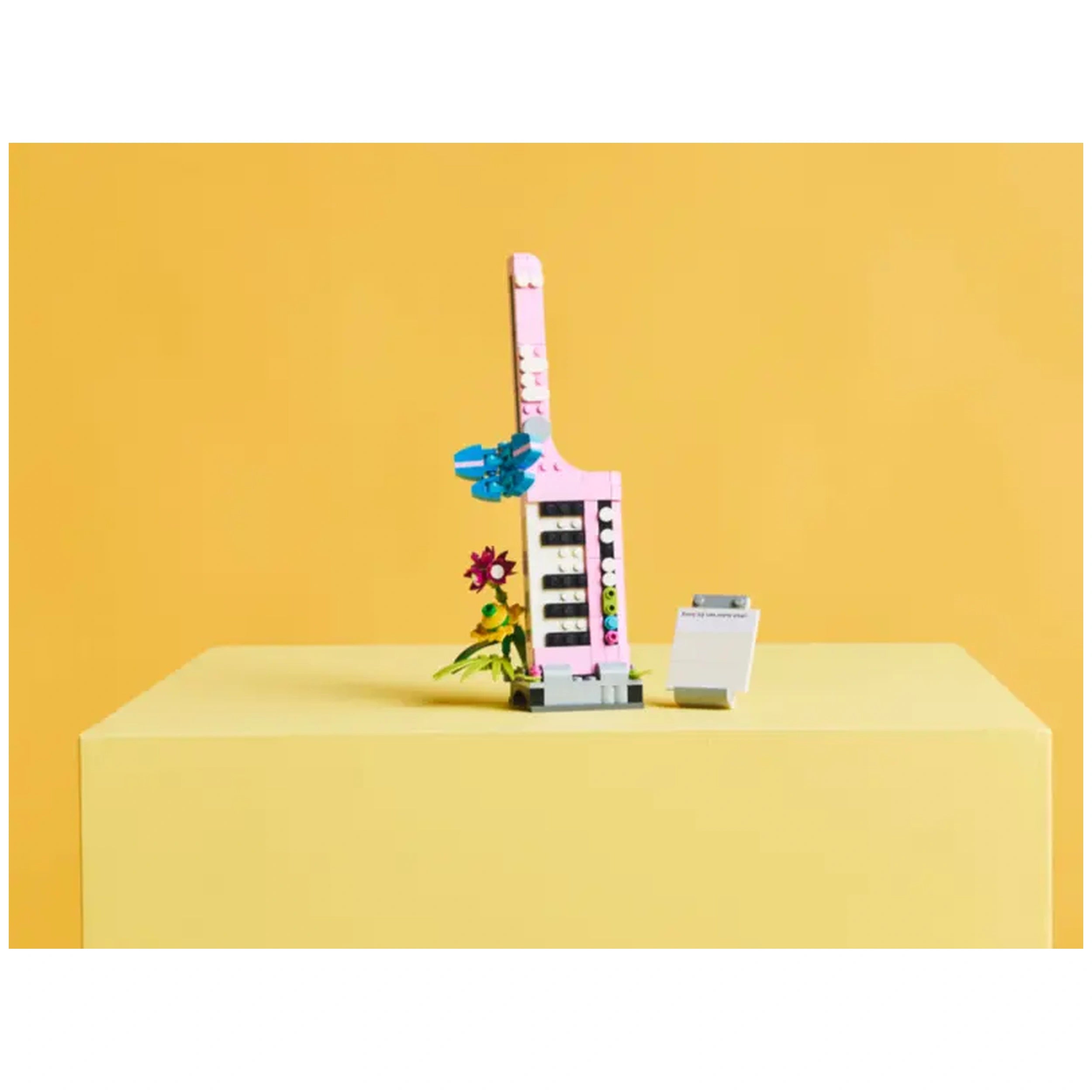 LEGO Creator 3in1 Typewriter with Flowers set, featuring a pink typewriter with colorful brick flowers and a small paper pad on a yellow background.
