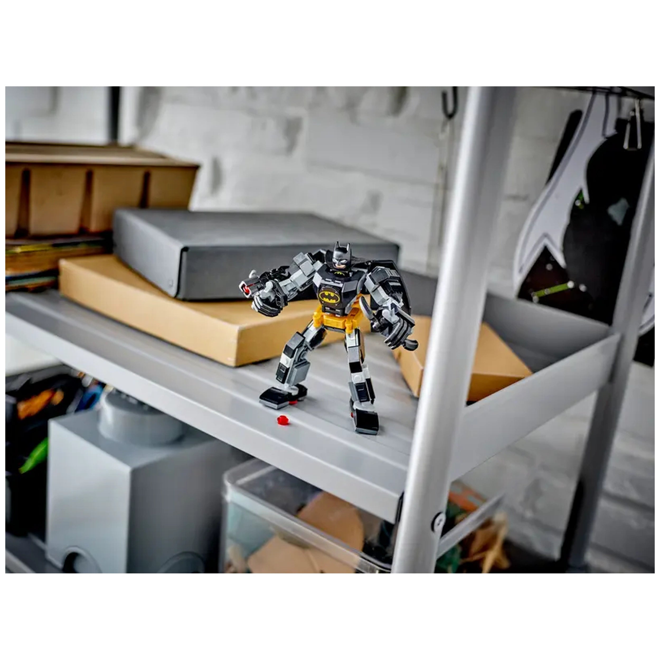 Batman mech armor toy stands confidently on a gray shelf surrounded by stacked boxes, with colorful containers beneath it, showcasing a playful and organized space.