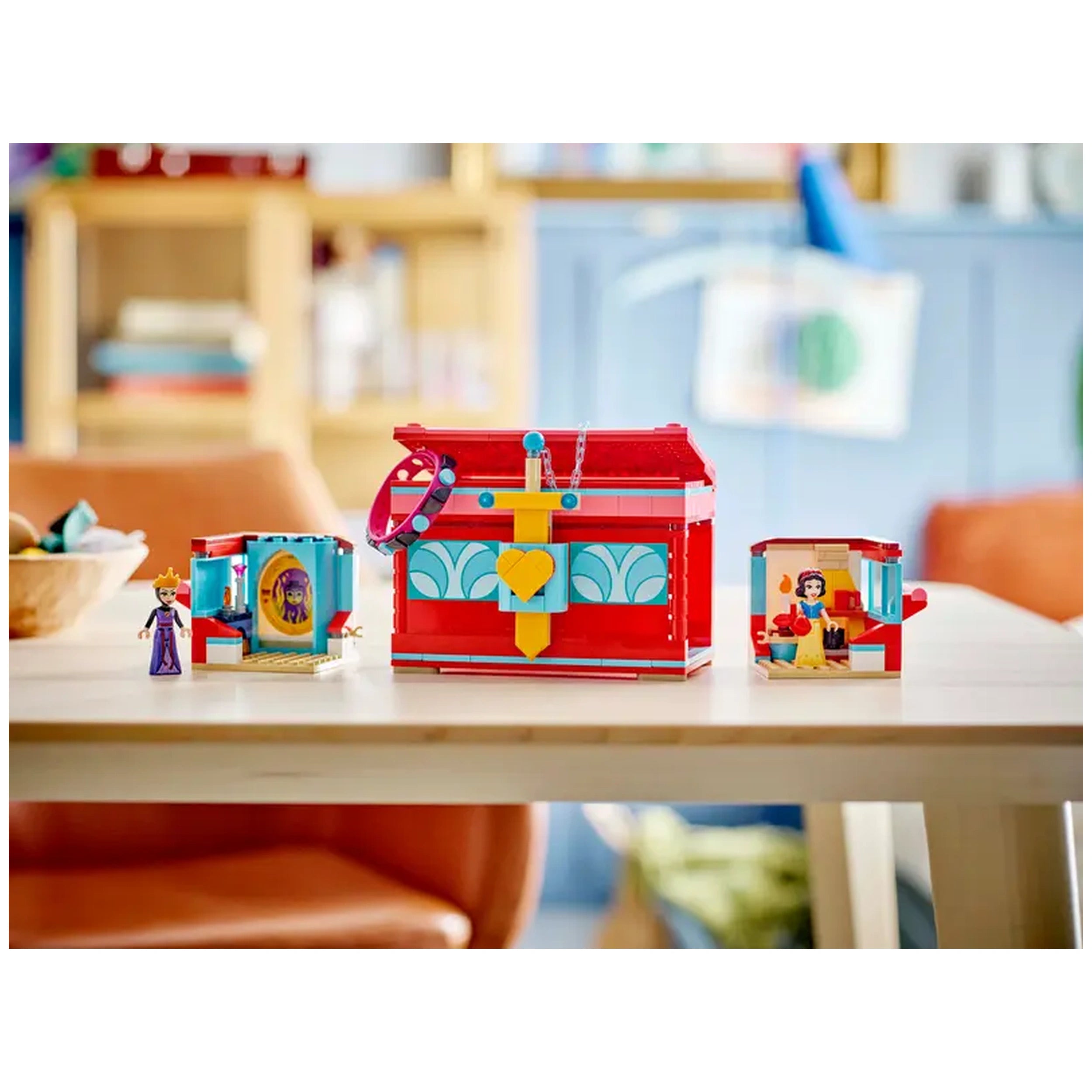 Colorful LEGO® Disney Snow White's Jewelry Box set displayed on a wooden table, featuring two mini-dolls: Snow White and the Evil Queen, on either side of a vibrant red jewelry box with a heart design and a lockable lid.