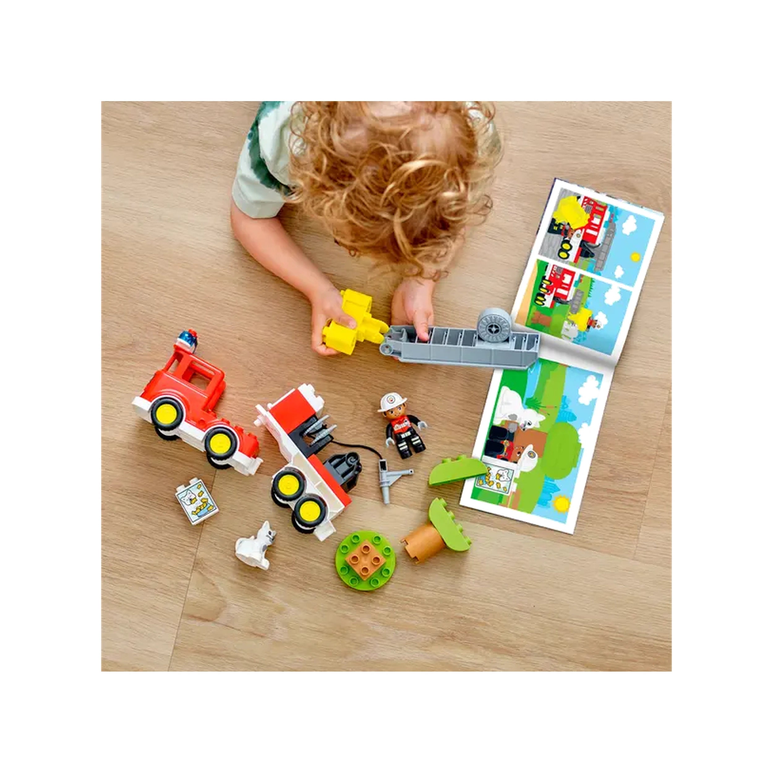 Young child with curly hair playing with a LEGO® DUPLO® fire truck set, surrounded by colorful pieces, instruction booklet, and a toy figurine.