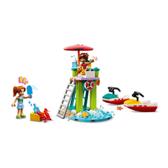Two mini-dolls play on a colorful lifeguard tower with a red umbrella, surrounded by water scooters, seashells, and a crab stealing an ice pop.