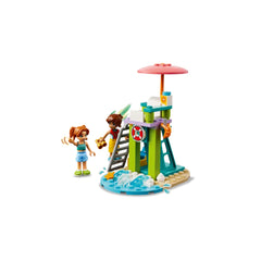 Two mini-dolls, Leo and Candi, play near a colorful lifeguard tower with a pink umbrella, surrounded by water elements and beach accessories.