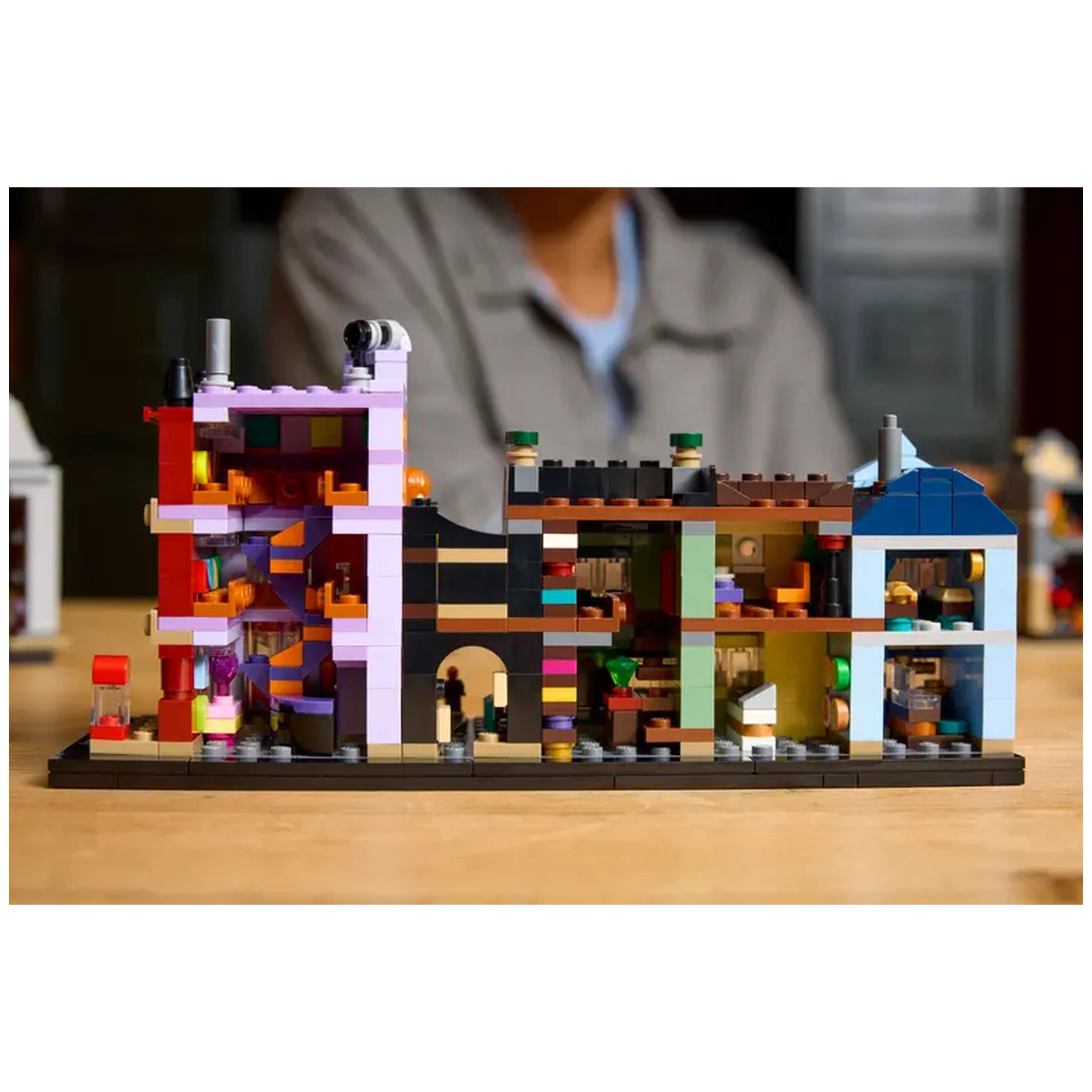 Microscale LEGO® Harry Potter™ Diagon Alley™ set displaying colorful wizarding shops with intricate interior details on a wooden table.