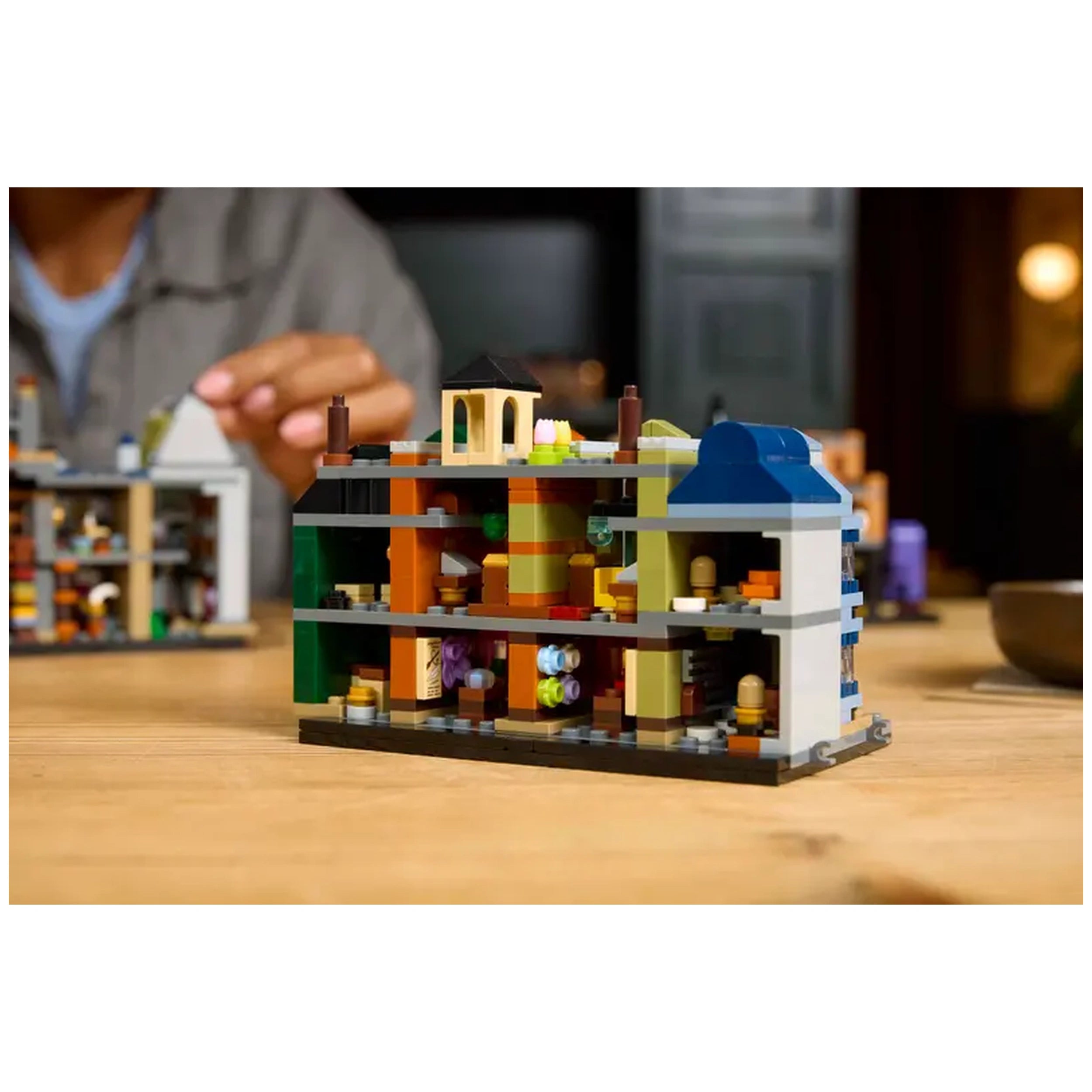 Microscale LEGO® Harry Potter™ Diagon Alley™ building featuring colorful shops and intricate interiors, displayed on a wooden table.
