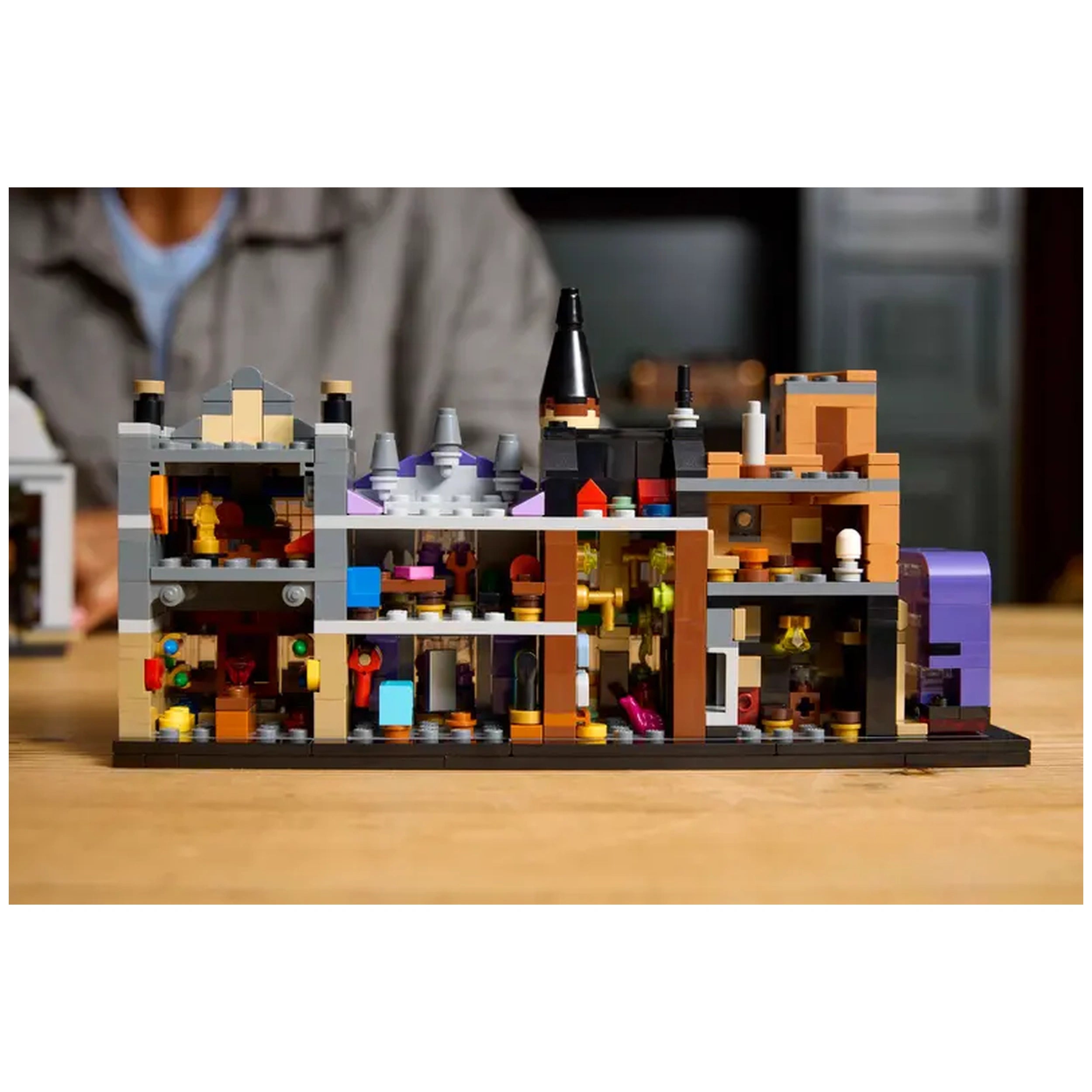 Colorful LEGO® Harry Potter™ Diagon Alley™ construction set displays intricate microscale buildings, including shops like Ollivanders™, with detailed interiors and whimsical design elements, set against a wooden background.