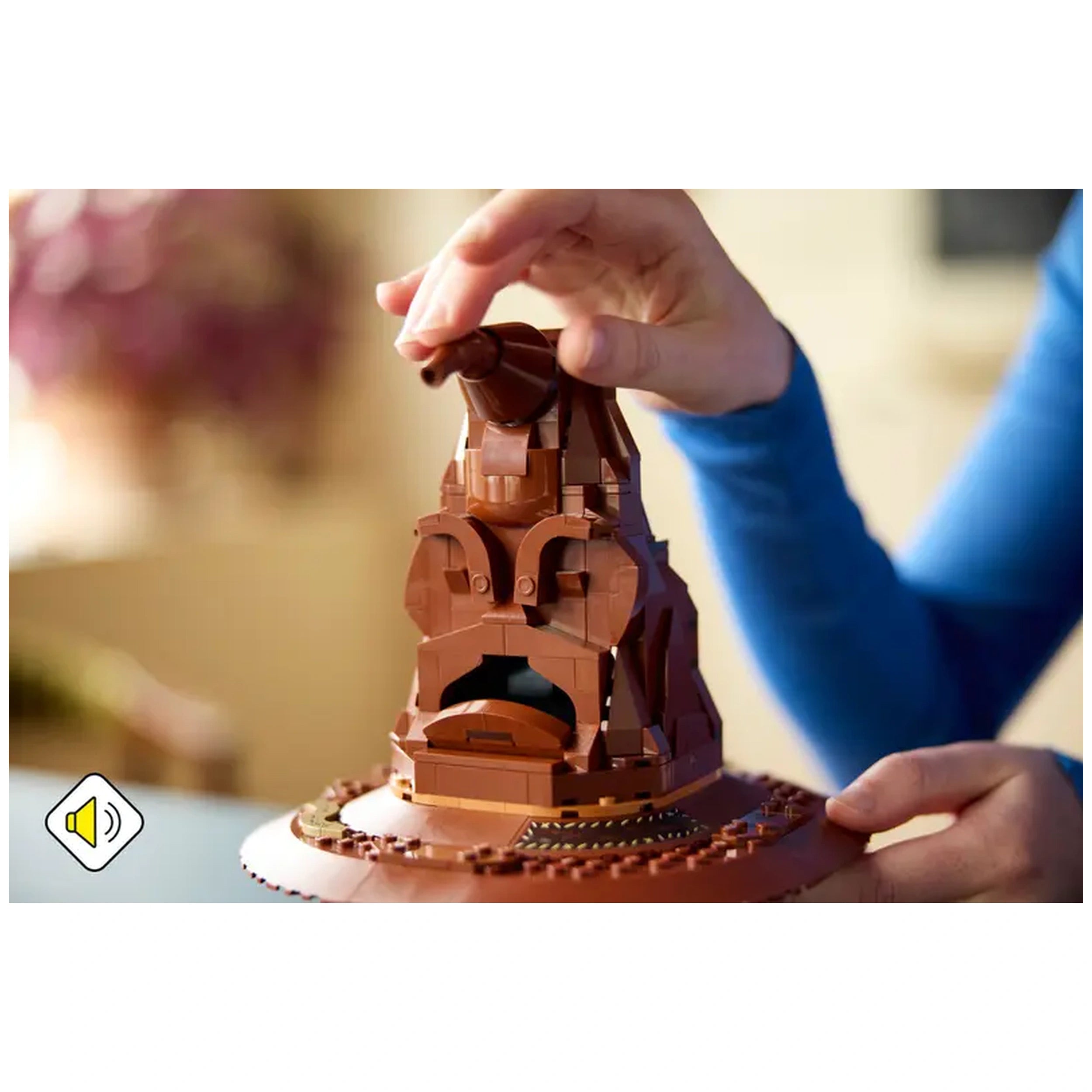 Hand interacting with the LEGO Harry Potter Talking Sorting Hat, a brown construction set with a detailed face, atop a round display base.