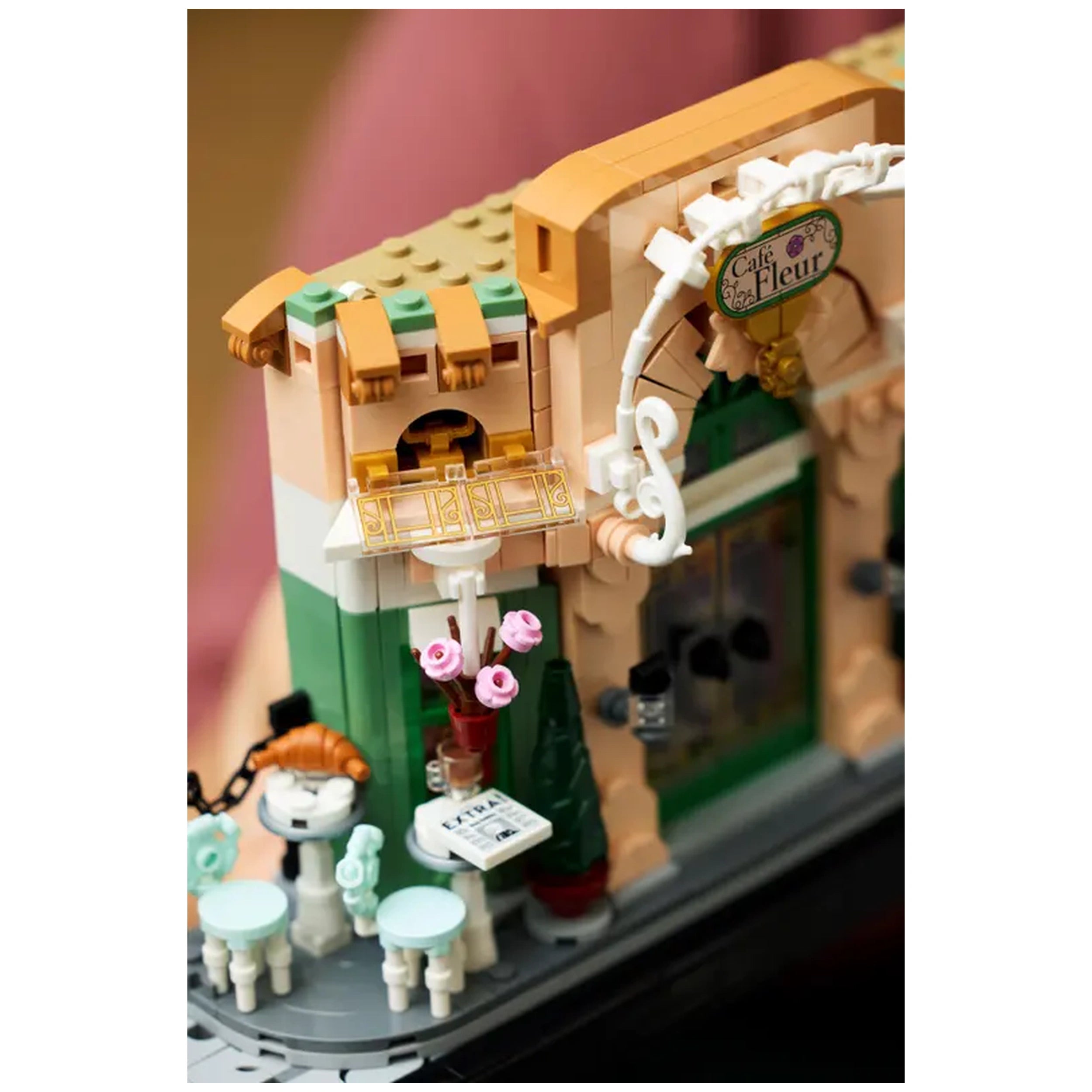 Charming LEGO® French Café facade with a pink flower pot, a quaint outdoor table, and green decorative elements.